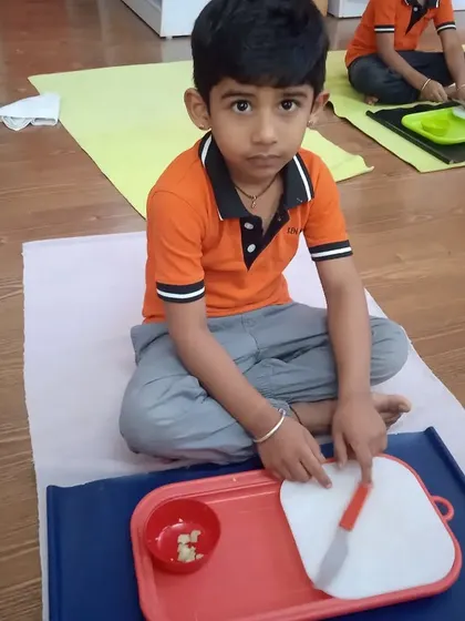 A young boy is focused on chopping a banana, a practical life skill that builds confidence and coordination. We use child-safe tools to ensure they can participate in food preparation safely and effectively.