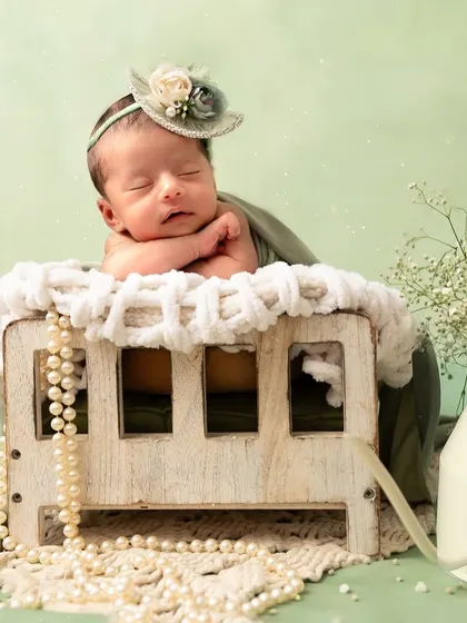 The same miniature bed is used here for a completely different feel. The baby is posed with her hands under her chin, wearing a lovely little hat and surrounded by pearls.