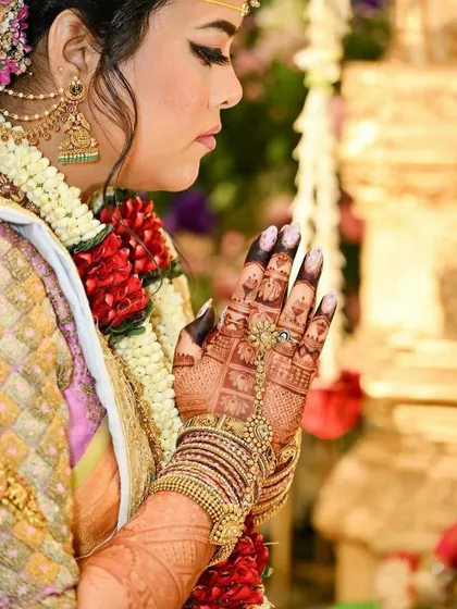 A close up of a bride's hands during a ceremony, showcasing the beautiful dark stain of her back hand mehndi. The color provides a stunning contrast with her jewelry.