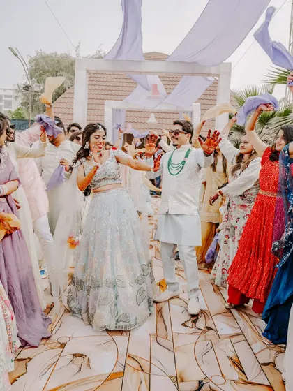 The couple's grand dance entrance at their Haldi. This shot captures Rahul and Riya leading the celebration, with guests waving colorful cloths in the air, creating a vibrant and dynamic scene.