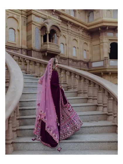 The bride looks like a queen as she ascends the grand, curved staircase of the palace, her deep purple lehenga trailing elegantly behind her.