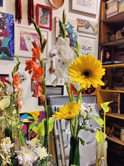 A vibrant corner of the studio, filled with flowers, books, and a gallery wall of colorful artwork.