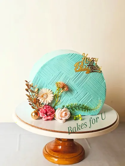 A modern cake-top-forward design with a textured turquoise finish. The cake is elegantly decorated with dried flowers and gold accents.