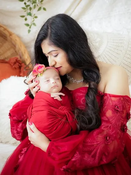 There is no role more essential than motherhood. This tender moment captures a new mother in a beautiful red gown, holding her swaddled newborn close.