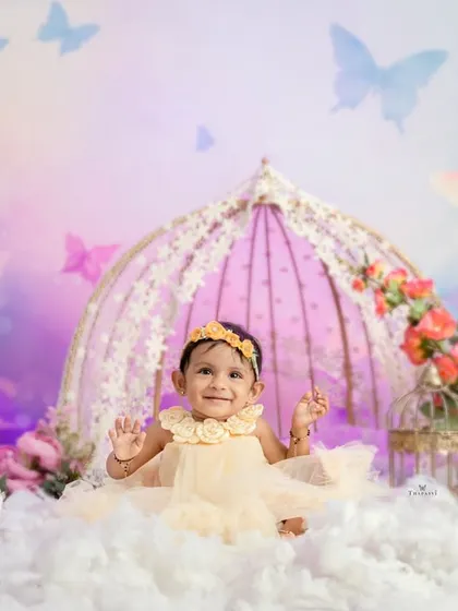 A dreamy butterfly-themed first birthday shoot. The birthday girl sits among fluffy clouds and a beautiful birdcage prop, with butterflies fluttering all around.