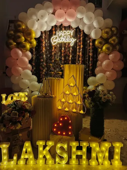 An intimate and warm birthday decoration for Lakshmi, featuring a pink, white, and gold balloon arch and an array of beautiful props.