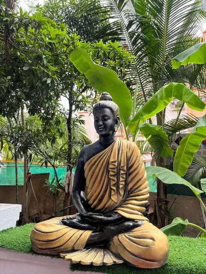 The sitting Buddha sculpture placed on artificial turf, demonstrating its versatility for gardens, patios, or balconies. The detailed folds of the robe are clearly visible.