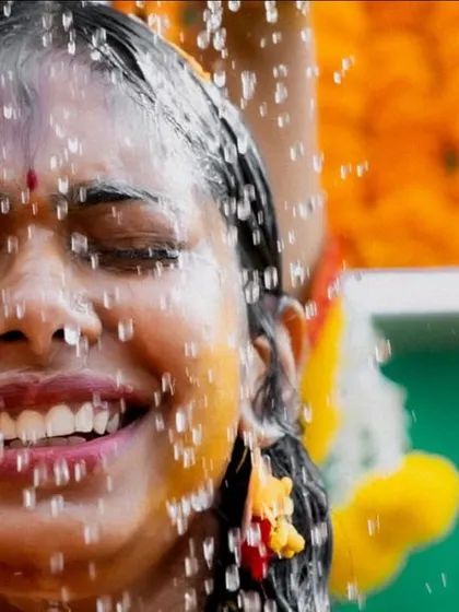 A close-up of a bride's face during the Haldi ritual, her expression a mix of laughter and joy as she's showered with water. This is a raw, real, and beautiful candid moment.
