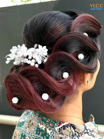An intricate updo with swirls of burgundy and black hair, accented with pearl pins and a crystal hair accessory. This is a perfect style for a glamorous wedding reception.
