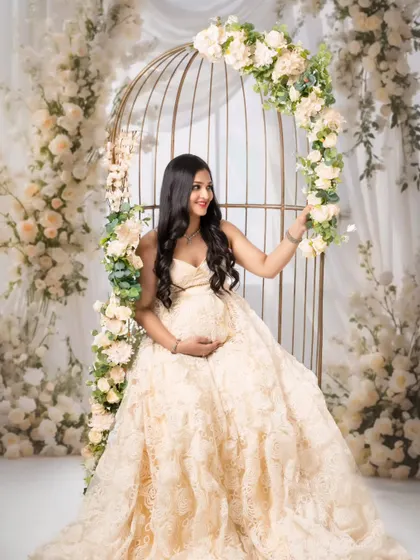 A mom-to-be looking like a fairy-tale princess, seated on a floral-adorned birdcage swing in a beautiful lace gown.