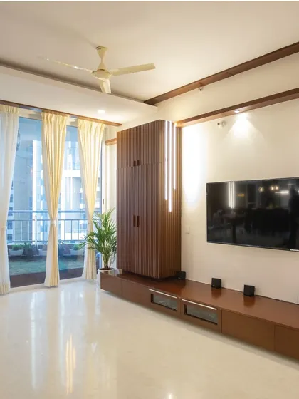 Another angle of the modern living room, showing the comfortable seating arrangement and the view of the balcony. The dark wood accents on the ceiling and TV unit provide a warm contrast to the bright, airy space.