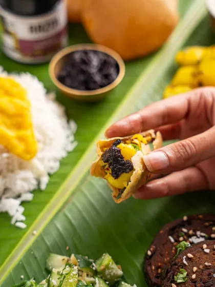 A hand enjoying a bite of food with Aazol chutney. This action shot shows the product in use in a relatable, traditional meal setting.