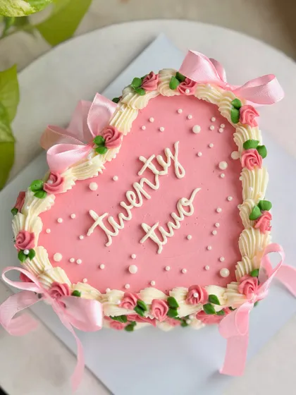 A beautiful overhead shot of the pink heart-shaped cake for a 22nd birthday, detailed with buttercream roses, pearls, and satin bows.