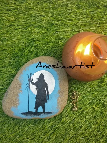 A silhouette of Lord Shiva painted on a smooth river stone, placed next to a candle for a serene evening pooja. This is a simple yet profound piece of spiritual art.