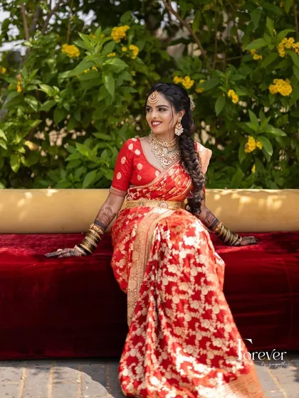 A full-length view of the bride on a red sofa, her beautiful red and gold saree spread out around her.