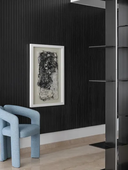Even transitional spaces like a foyer can be a place for art. Here, a bold, sculptural chair in a striking blue is set against a black fluted wall with abstract art, creating a powerful and memorable first impression.