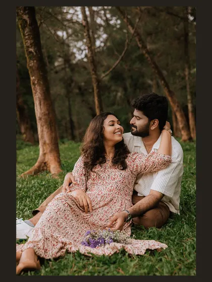 A sweet and relaxed portrait of a couple sitting in the grass, surrounded by trees.