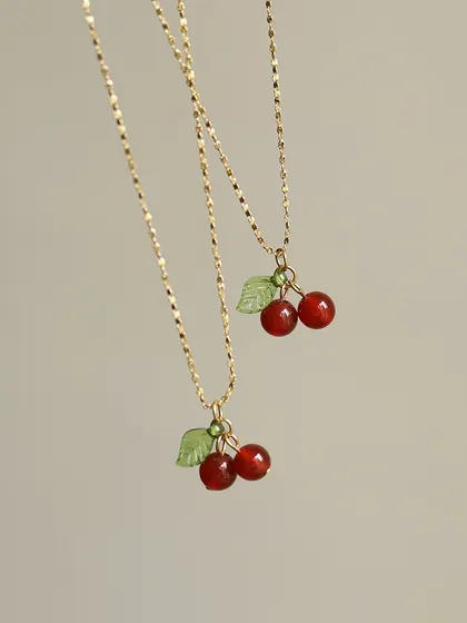 A whimsical and cute necklace featuring a small cherry charm with red beads and a green leaf. This playful piece is made from high-quality materials and adds a fun touch to your style.