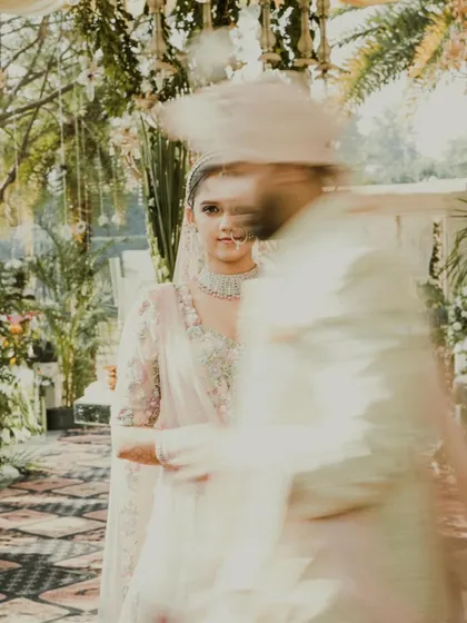 An artistic motion-blur shot, with the bride in sharp focus as the groom walks past. It creates a dynamic, dreamlike effect.