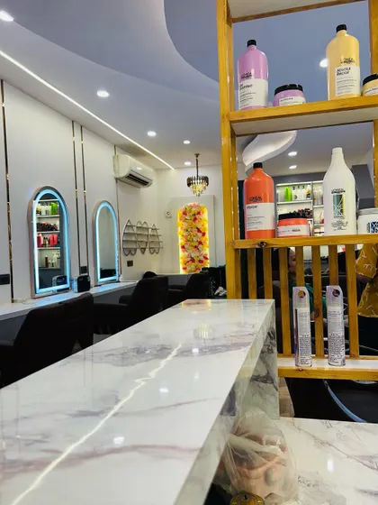 A real-life shot of a completed salon reception counter. The glossy marble finish on the counter, combined with the custom shelving and view of the well-lit styling stations, gives a great sense of the final quality.