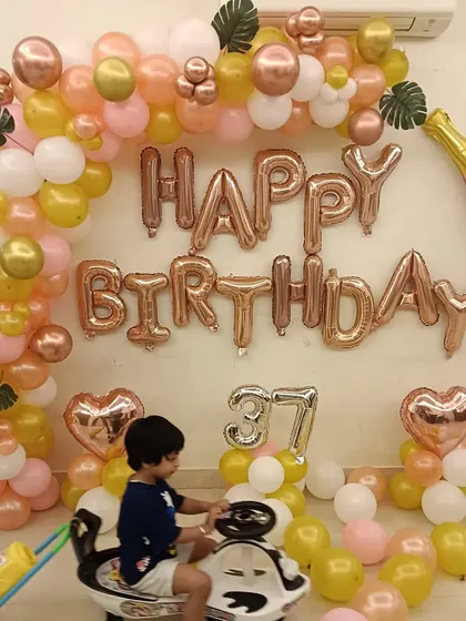 A warm and cheerful home decoration in rose gold and yellow tones. This setup includes a balloon arch, "Happy Birthday" foil letters, and a champagne bottle balloon.