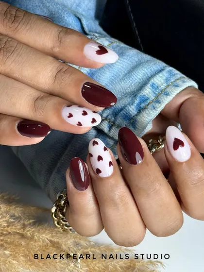 A romantic and chic design with deep dark maroon nails paired with a milky white base and tiny, hand-painted hearts. This look is perfect for a date night or any time you want to feel gorgeous.