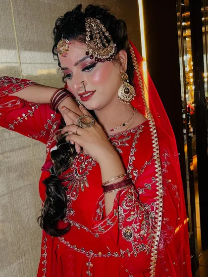A stunning Pakistani bridal look, rich in tradition and elegance. This style features a vibrant red outfit, elaborate gold jewelry including a jhoomar and passa, and dramatic eye makeup with a flawless base, capturing the grandeur of a traditional Nikah ceremony.