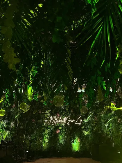 A stunning entrance designed to feel like a lush, tropical jungle. We covered the walls and ceiling with dense greenery and used a custom neon sign to welcome guests to this wild and chic cocktail party.
