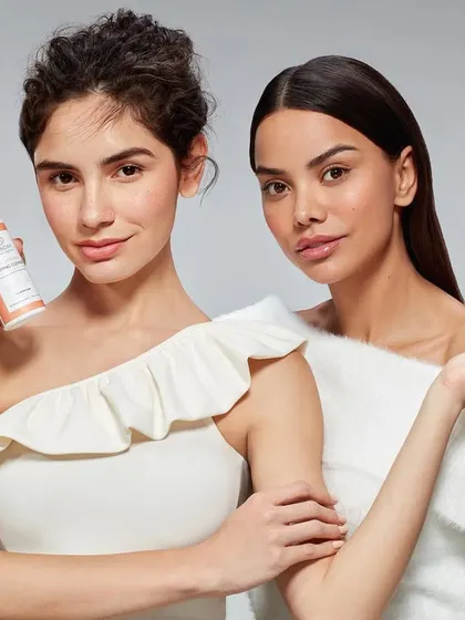 A group portrait for Skinora Cosmetics featuring two models. One model holds a foaming cleanser while the other demonstrates its texture, creating a dynamic shot that showcases both the product and its application.