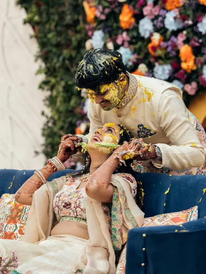 The groom playfully smears haldi on the bride's face during their ceremony. This candid action shot is filled with energy and happiness.