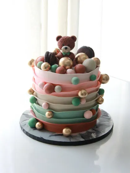 A playful baby shower cake with colorful ruffles and a cute teddy bear on top.