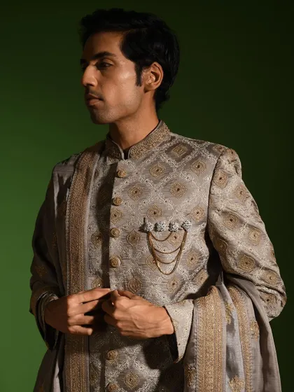 A side profile of the steel grey sherwani, showing how the intricate pattern flows across the garment. The precise tailoring around the shoulders and collar ensures a sharp, defined silhouette.