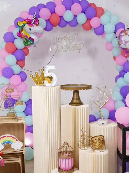 A close-up of a unicorn-themed setup, showing the colorful balloon arch and whimsical props like a mini Ferris wheel and birdcage.