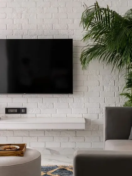 A wider view of the TV room, showing the balance between the textured brick wall, the sleek media setup, and the comfortable seating. The large plant brings an organic element that softens the minimalist design.