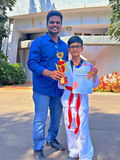 This red-and-black belt student shows off his medal and trophy, representing a higher level of achievement in Taekwondo.