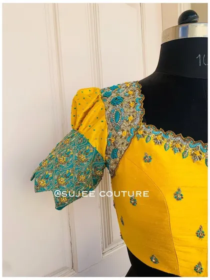 A side view of the yellow puff sleeve blouse. This angle shows the volume of the sleeve and the detailed embroidery on the teal-colored cuff, which adds a unique design element.