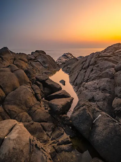 A vertical composition of a rocky shoreline at sunset, focusing on the warm glow and the interesting shapes of the rocks.