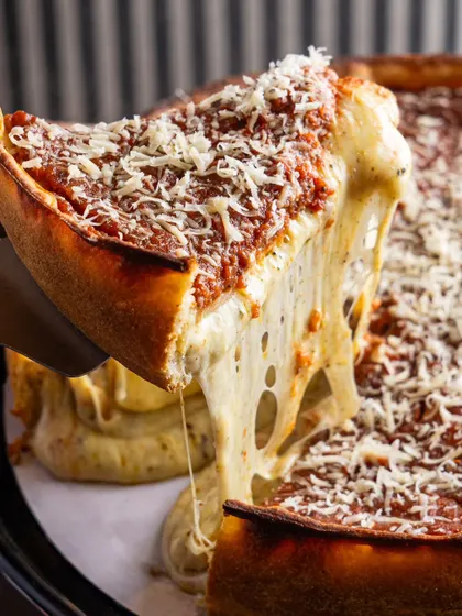 A close-up of a Chicago-style deep-dish pizza slice. The lighting is designed to highlight every layer, from the crust to the sauce and cheese.