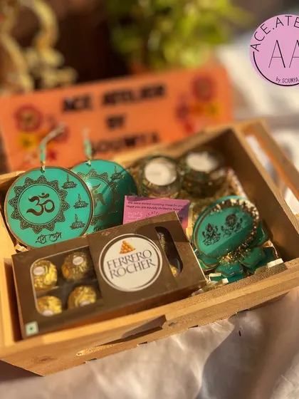 This Diwali hamper in a wooden tray features beautiful teal resin decor, including Om hangings and Lakshmi Ganesh pieces.