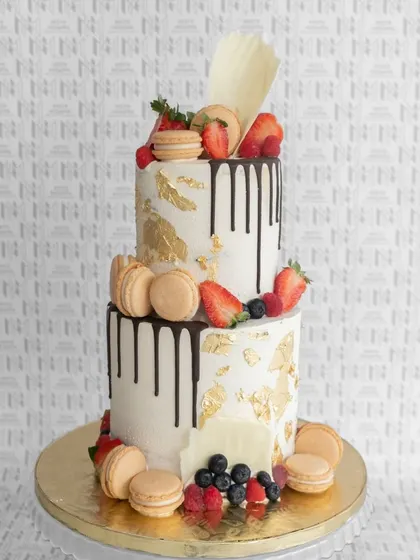 A two-tiered drip cake with gold leaf, macarons, and a beautiful assortment of fresh berries.