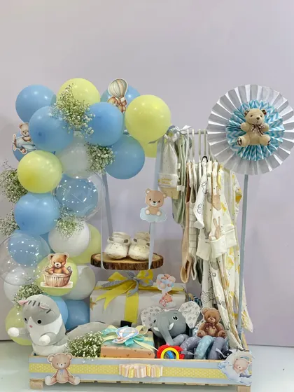 This grand display was created to welcome a new baby. It features a clothing rack with adorable outfits, soft toys, baby shoes, and a beautiful balloon arch, making it a practical and visually impressive gift for new parents.