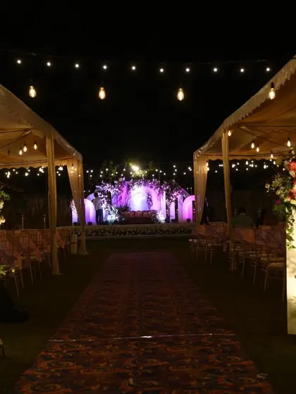 An enchanting outdoor reception pathway lined with tents and leading to a beautifully lit stage in the distance, creating a sense of journey and grandeur for the guests.