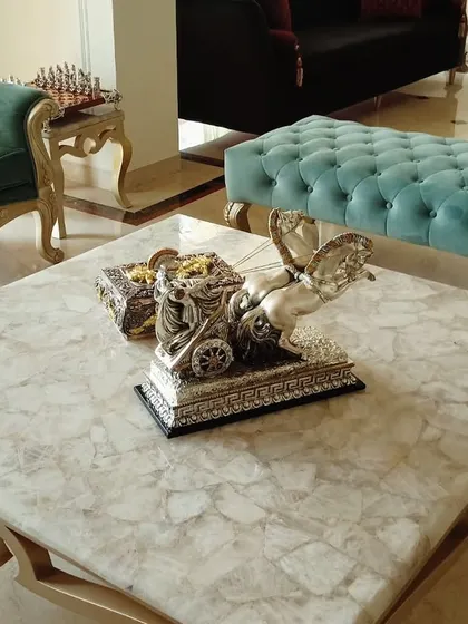 A detailed shot of a living room featuring a custom marble-top coffee table. In the background, you can see a plush green velvet armchair and a tufted turquoise bench, demonstrating our use of rich textures and materials.