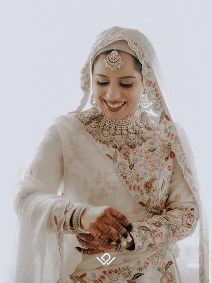 A happy Muslim bride looking down at her hands, a candid moment capturing her joy and the intricate details of her embroidered outfit.