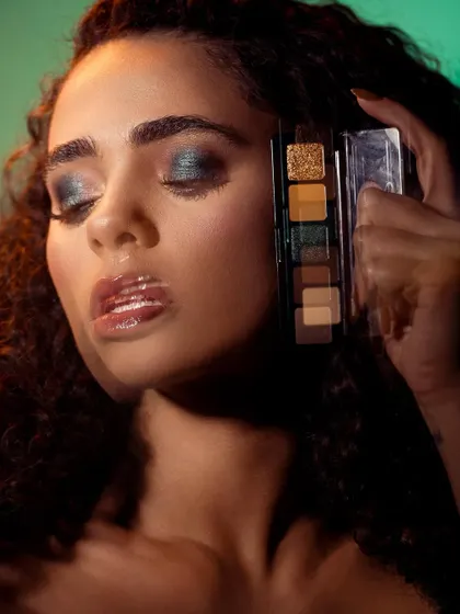 A glamorous and sensual shot featuring a model with glossy lips and shimmering eyeshadow. The motion blur on her hand adds a dynamic element, as if caught in a fleeting moment. The lighting creates a beautiful glow on her skin, emphasizing the glittery, high-impact makeup.