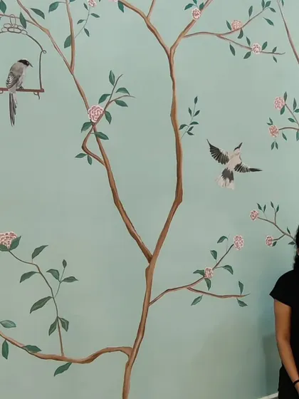 A beautiful shot of a completed Chinoiserie-style mural with a soft blue background, featuring delicate branches, birds, and pink flowers.
