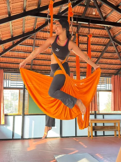 A student strikes a confident pose in the orange aerial silk, embodying the grace and strength we build in these classes.