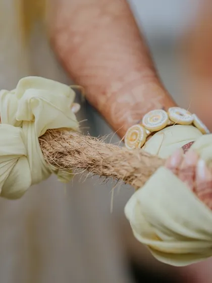 A symbolic detail shot of the couple's hands tied to the rope for the tug-of-war game, representing their playful bond.