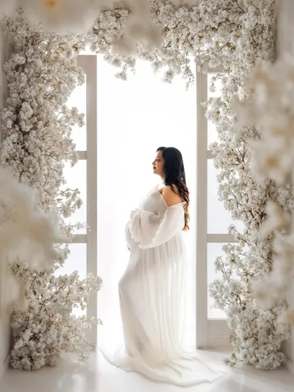 This is the single most important photo to capture your pregnancy glow. Here, a stunning mommy-to-be stands in a flowing white gown, framed by a beautiful arch of white blossoms, creating a timeless and ethereal maternity portrait.