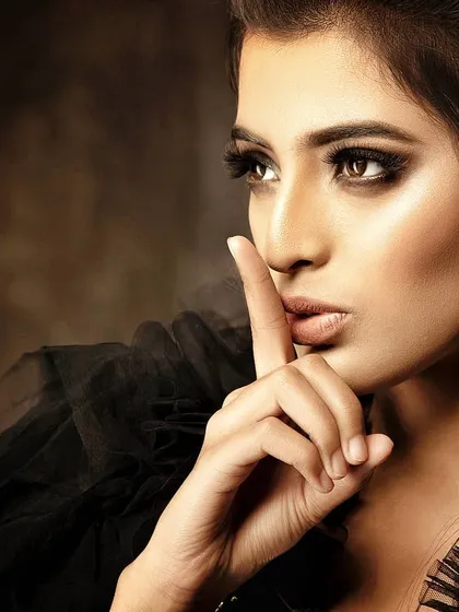 A close-up portrait with a gesture that conveys silence and intensity. The warm, directional lighting and dark background make this a powerful and intimate beauty shot.